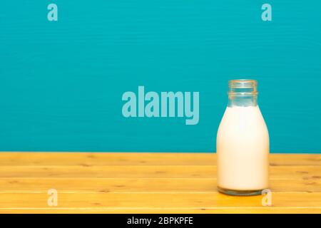 Frische, cremige Milch in einem Drittel pint Glas Milch Flasche, auf einen hölzernen Tisch gegen einen hellen Teal gemalten Hintergrund Stockfoto