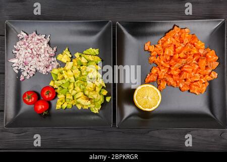 Scheiben Lachs, Zwiebel und Avocado auf Tellern auf schwarzem Holzhintergrund Stockfoto
