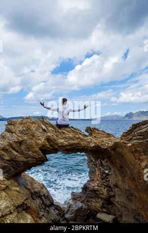 Der Mensch bewundert das Meer auf einem schönen Steinfelsen mit einem Bogen, Griechenland Stockfoto