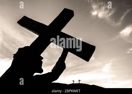 Bronzestatue von Jesus sein Kreuz trug, auf dem Weg zu seiner Kreuzigung. Ideal für Ostern, Auferstehung und andere. Himmel mit Wolken auf Bac Stockfoto