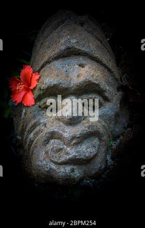 Alte balinesischer Stein mit einem roten Hibiskus Blume hinter dem Ohr, Ubud, Bali, April, 14 2018 Stockfoto
