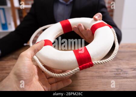 Geschäftsleute halten ein Rettungsring Holding in die Hände über Holz- Schreibtisch Stockfoto