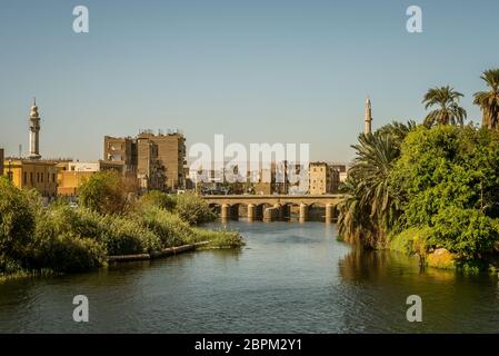 Ägyptischen Stadt im Sonnenuntergang mit zwei minaretes und eine Brücke. Eine Ansicht von einer Kreuzfahrt auf dem Nil, Ägypten. Oktober 27, 2018 Stockfoto