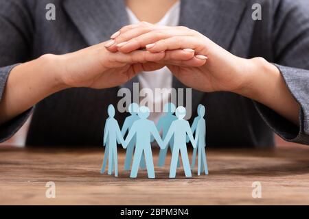 Close-up ist eine Geschäftsfrau, die schützende Hand blau Papier schneiden Sie menschliche Figuren bilden Kreis Stockfoto