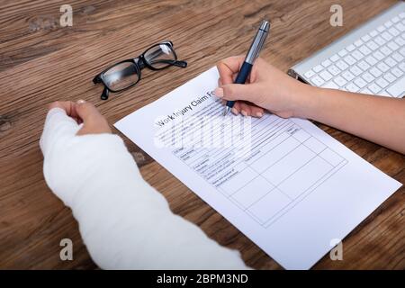 Nahaufnahme der Geschäftsfrau mit weißen Bandagen Hand Befüllen Arbeitsunfall Antragsformular auf hölzernen Schreibtisch Stockfoto