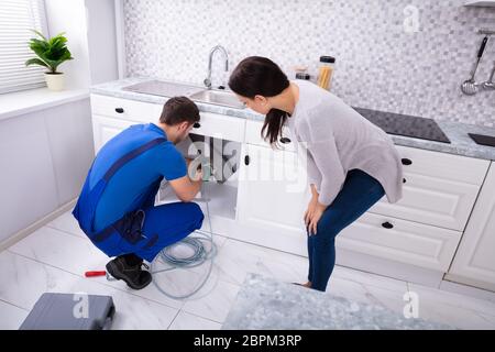Frau an männlichen Klempner Reinigung verstopfte Waschbecken Rohr mit durchlässigen Kabel in der Küche auf der Suche Stockfoto