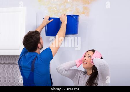 Frustriert Frau mit Heimwerker sammeln Wasser beschädigte Decke Blau Schaufel Stockfoto