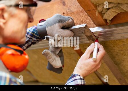 Mann in Googles eine Markierung auf Metall Rahmen auf unfertige Dachgeschoss Decke. Dachboden Isolierung und Renovierung Stockfoto