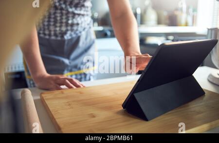 Frau, die den Touchscreen auf einem digitalen Tablet in der Küche zu Hause auf einem Schneidebrett verwendet Stockfoto