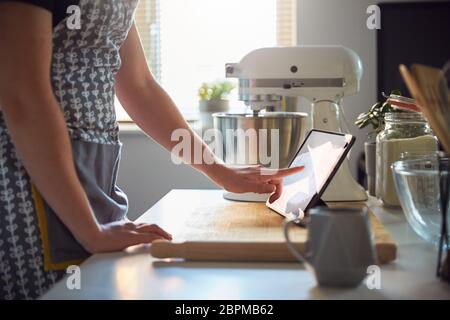 Frau, die den Touchscreen auf einem digitalen Tablet in der Küche zu Hause auf einem Schneidebrett verwendet Stockfoto