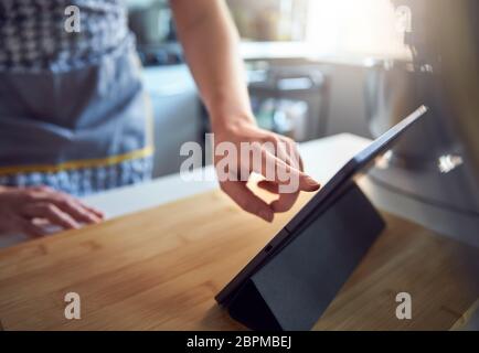Frau, die den Touchscreen auf einem digitalen Tablet in der Küche zu Hause auf einem Schneidebrett verwendet Stockfoto