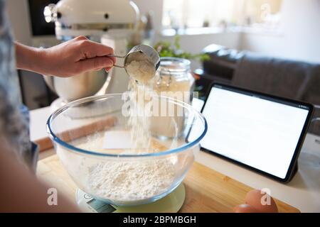 Frau, die Blume in eine Mischschüssel zu Hause gießt, schließen Sie sich an. Auf digitalen Skalen Stockfoto