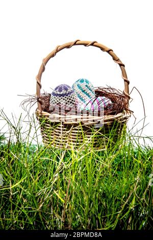 Bunte Ostereier im Nest auf Holz- Korb am grünen Gras auf weißem Hintergrund. Frohe Ostern Stockfoto