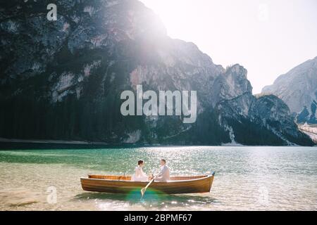 Frisch vermählte fahren in einem Holzboot auf dem Pragser See in Italien. Hochzeit in Europa, am Pragsersee. Brautpaar - der Bräutigam Reihen mit hölzernen Ruder Stockfoto