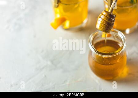 Löffel für Honig über Glas vor zwei Gläsern Honig Bourbon Cocktail mit Rosmarin-Sirup oder hausgemachten Whisky sauer mit Orangenschale und Rosmarin Stockfoto