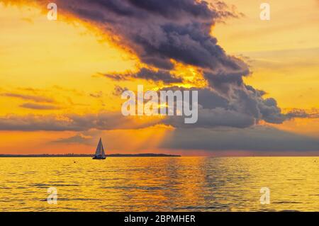 Einen wunderschönen Sonnenuntergang am Meer mit einem Segelboot und dramatische Wolken Stockfoto