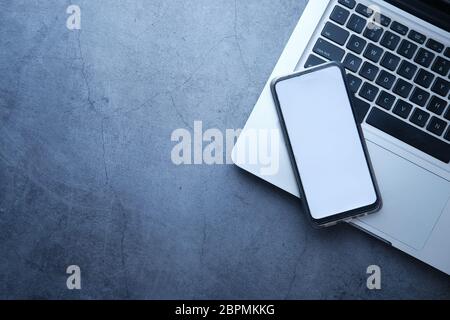 Draufsicht auf Smartphone mit leerem Bildschirm und Laptop auf grauem Hintergrund Stockfoto