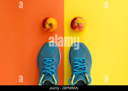 Blaue Sneaker und Äpfel auf gelborangenem Hintergrund. Das Konzept eines gesunden Lebensstils, des täglichen Trainings und einer guten Ernährung. Flaches Lay, Kopierbereich. Stockfoto