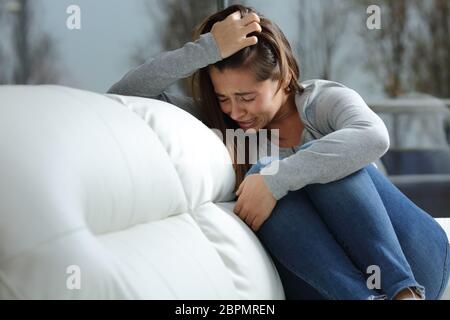 Trauriges Mädchen weint verzweifelt allein sitzen auf einer Couch zu Hause in einem dunklen Wintertag Stockfoto