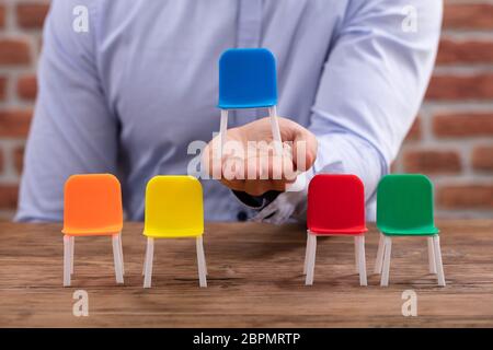 Person's Hand, die blauen Stuhl in der Nähe der bunten Stühlen auf Schreibtisch Stockfoto
