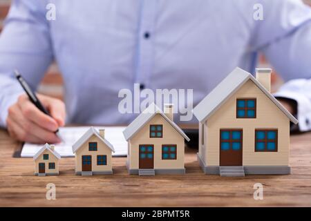 Nahaufnahme der Geschäftsmann Berechnung Rechnung mit Taschenrechner mit Haus Modell auf Büro Schreibtisch Stockfoto