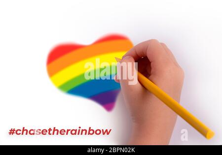 Das Konzept der Verfolgung des Regenbogens. Eine Hand mit einem Bleistift zeichnet ein Herz in Regenbogenfarben. Inschrift chasetherainbow. Stockfoto