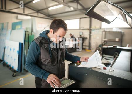 Der Techniker der Druckerei arbeitet an der Laser-CNC-Computer-numerischen Steuerungs- und Schneidemaschine Stockfoto