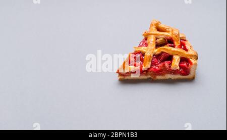 Erdbeer- und Rhabarber-Tortenscheiben in Nahaufnahme auf grauem, nahtlosem Hintergrund. Minimalistisches Bild eines einzelnen Stücks Kuchen. Deutscher Rhabarber Kuchen. Stockfoto