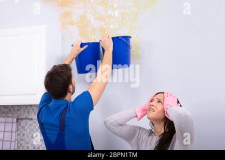 Frustriert Frau mit Heimwerker sammeln Wasser beschädigte Decke Blau Schaufel Stockfoto