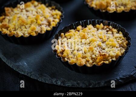 Kleine und leckere Apfelkuchen oder Apfelbrösel auf schwarzem Hintergrund. Apfeltarte. Stockfoto