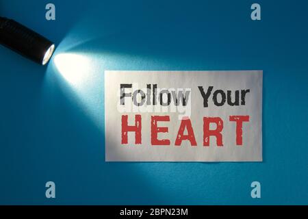 Folgen Sie Ihrem Herzen - Inschrift auf einer weißen Karte im Lichtstrahl Stockfoto