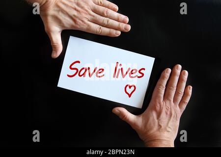 Die Hände des Mannes halten eine Karte mit der Aufschrift Save Lives auf schwarzem Hintergrund Stockfoto