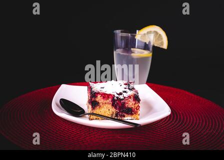 Hausgemachter Kuchen mit Waldfrüchten auf einem Teller mit einem Glas erfrischender Limonade mit Zitronenscheibe serviert Stockfoto