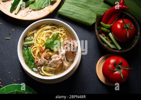 Asiatische Suppe, Nudeln und Huhn in Schüssel auf dunklem Hintergrund. Ansicht von oben flach. Stockfoto