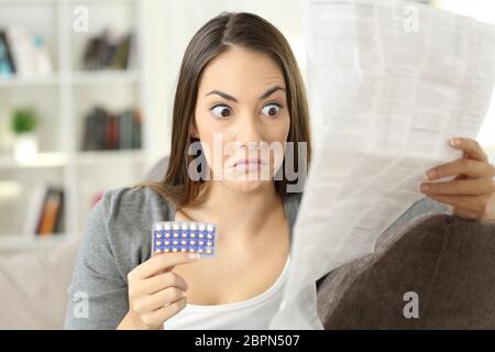 Porträt eines verwirrten Mädchens, das Kontraindikationen in einem Flugblatt mit Verhütungspillen liest, das auf einer Couch in einem Hausinneren sitzt Stockfoto