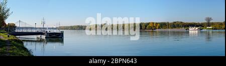 Blaue Donau mit Schiffsanlegestelle, Frachtschiff und sogenannter Rosenbrücke im Rücken bei Tulln, Österreich Stockfoto