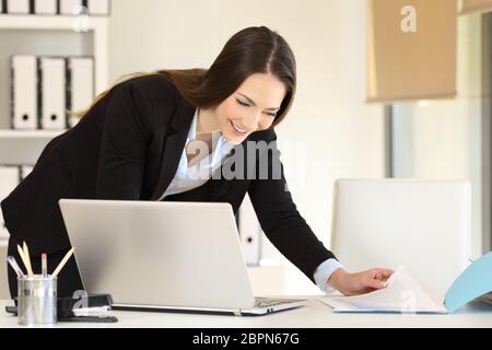 Happy Geschäftsfrau Vergleichen von Dokumenten online auf einem Schreibtisch im Büro Stockfoto