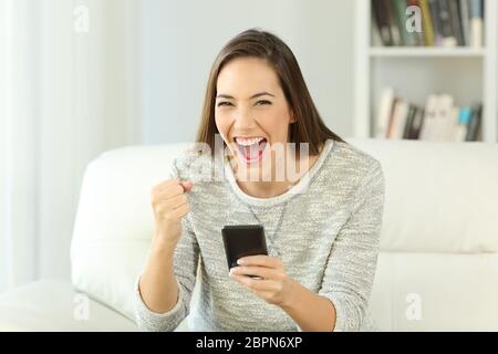 Vorderansicht Porträt einer aufgeregt Frau, die Telefon auf Sie sitzen auf einem Sofa im Wohnzimmer eines Hauses Interieur Stockfoto