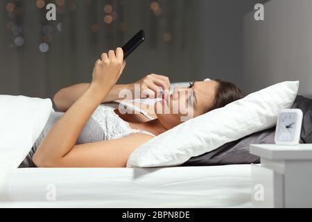 Nervöse Frau liest eine telefonische Nachricht auf einem Bett in der Nacht zu Hause Stockfoto