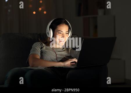 Happy girl elearning online mit einem Laptop in der Nacht auf einer Couch im Wohnzimmer zu Hause sitzen Stockfoto