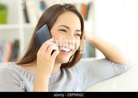 Glückliche Dame, die auf dem Handy spricht und zu Hause auf einem Sofa sitzt Stockfoto