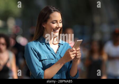 Smiley Mädchen mit einem Smartphone zu Fuß auf der Straße an einem sonnigen Tag Stockfoto