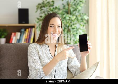 Blick nach vorne auf eine glückliche Frau zeigt einen schwarzen Bildschirm auf Linie und präsentiert ein neues Produkt in einem Haus-Interieur Stockfoto