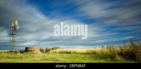 Langbelichtungs-Bild mit Windmühle und Damm und streifigen Wolken über dem Kopf Stockfoto