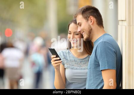 Paar Online-Medien-Inhalte in einem Smartphone auf der Straße stehen zu sehen Stockfoto