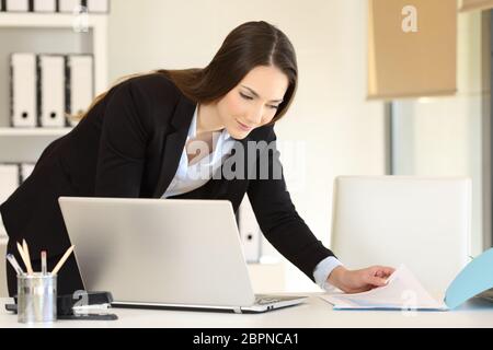 Büroangestellter arbeiten Vergleichen von Dokumenten online mit einem Laptop auf einem Desktop Stockfoto