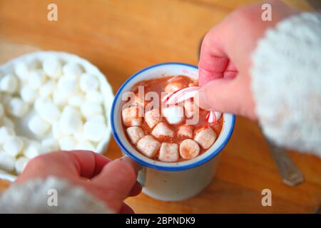 Hält eine Frau eine Zuckerstange in einem Becher heißer Schokolade mit Marshmallows Stockfoto