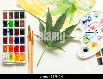 Set von Aquarellfarben, Kunstpinsel, Palette und leeres Album. Marihuana-Blatt. Cannabis offenbart Kreativität. Der Begriff der Kunst Stockfoto