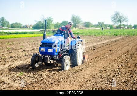 Ein Bauer auf einem Traktor bewirtschaftet ein Feld. Bodenfräsen, Zerbröckeln und Mischen. Lockern der Oberfläche, Anbau des Landes für die weitere Pflanzung. A Stockfoto