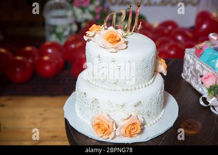 Auf dem Kuchen sind gelbe Blumen. Der Buchstabe U und R sind auf dem Kuchen in Gold geschrieben. Weißer zweistufiger Kuchen . Stockfoto
